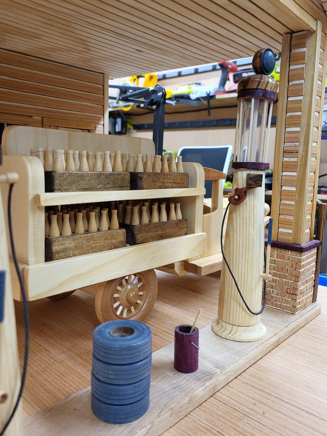 Wooden model of a vintage gas station with a truck, gas pumps, and tools; indoors.