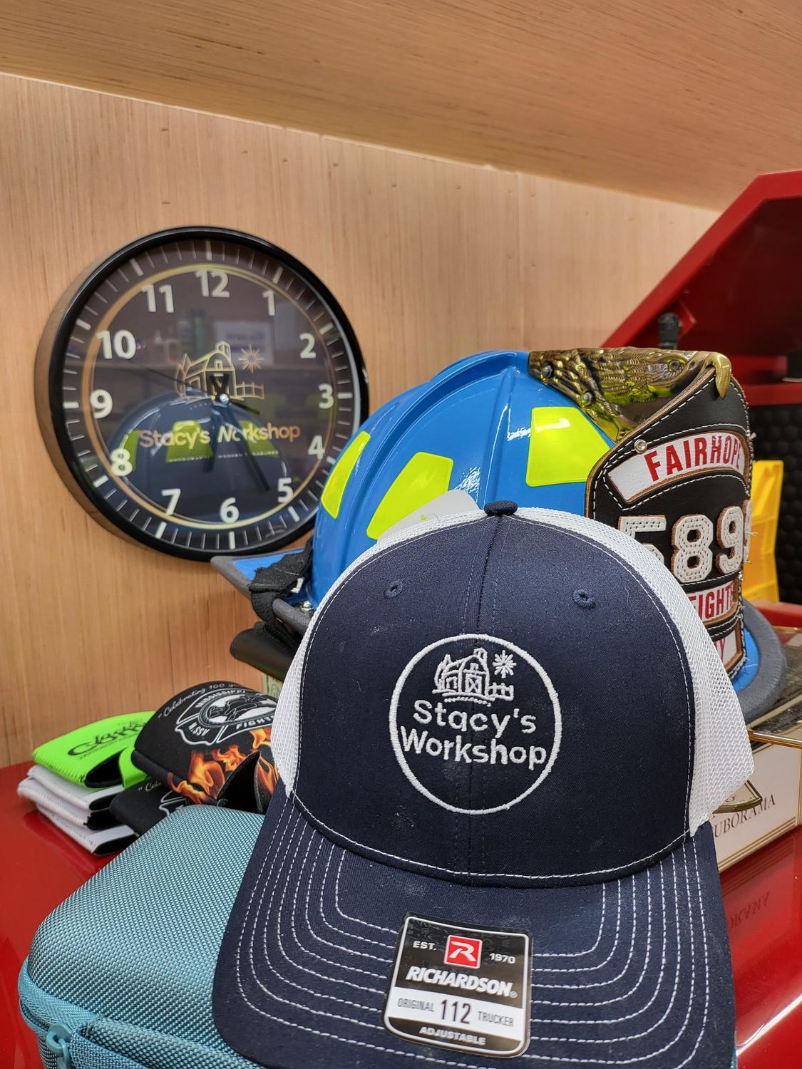 Stacy's Workshop ball cap in front of a clock, a firefighter helmet, and a racing sign.