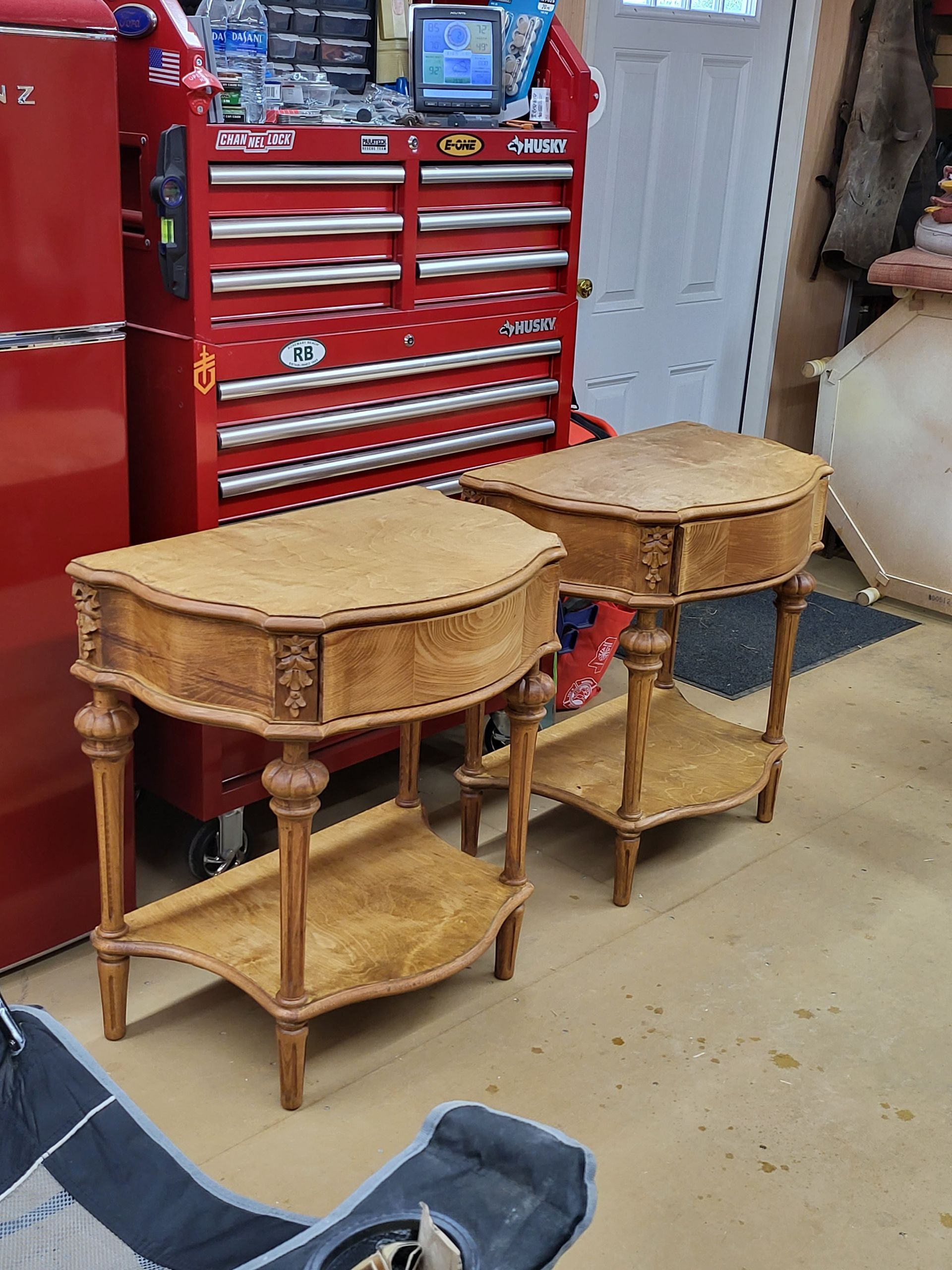 Two antique wooden bedside tables with ornate details, next to a red toolbox.