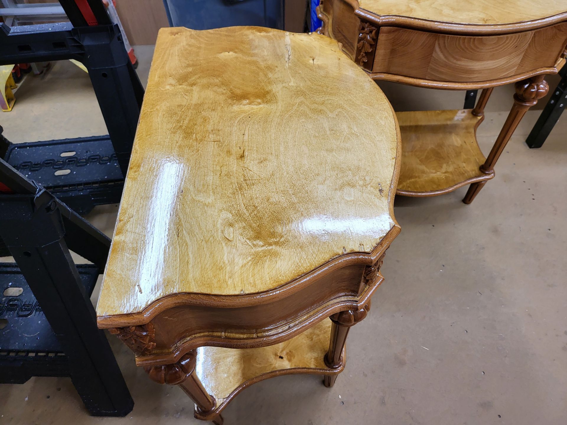 Refinished antique table, light wood grain, ornate dark trim, second similar table in background, workshop setting.