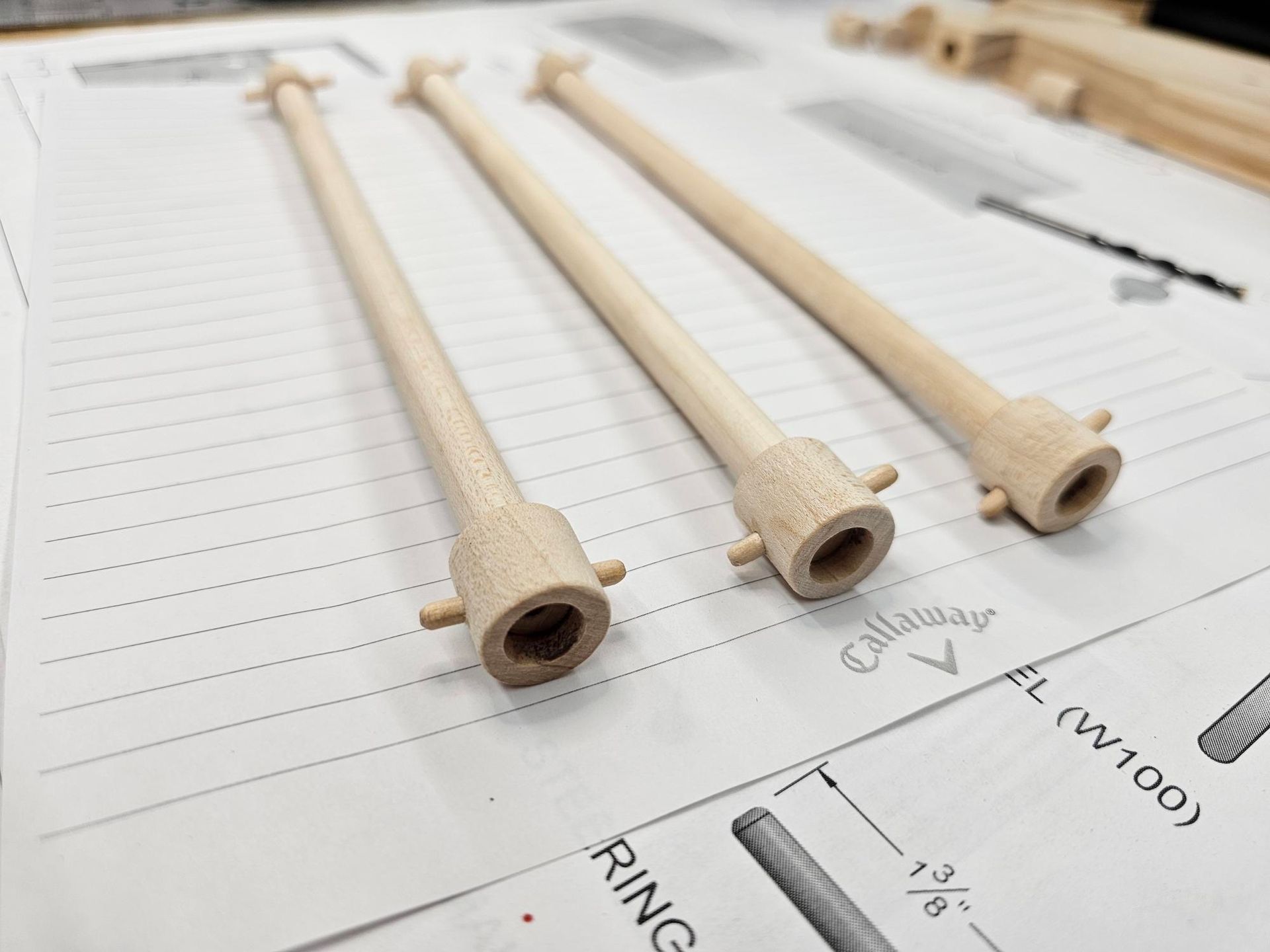 Three light-colored wooden spindles with flared ends and central holes, lying on a blueprint.