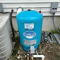 Blue Well-Rite water tank outside a building, with pipes and other equipment visible.