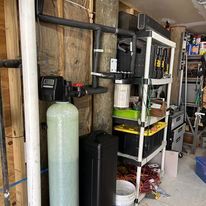 Water filtration system in a utility area with storage shelving and other equipment.