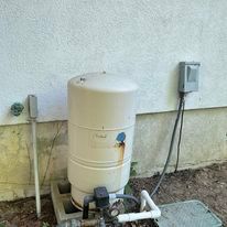 Water well pressure tank next to a wall with electrical components.