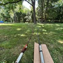 Two long metal objects on grass, one resting on cardboard, trees in background.