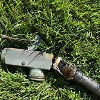 Damaged electrical cable and connector lying on green grass.