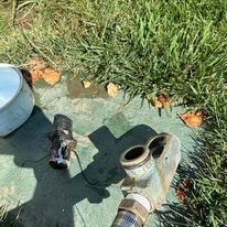 Irrigation system components on green surface near grass and a white container; partially disassembled.