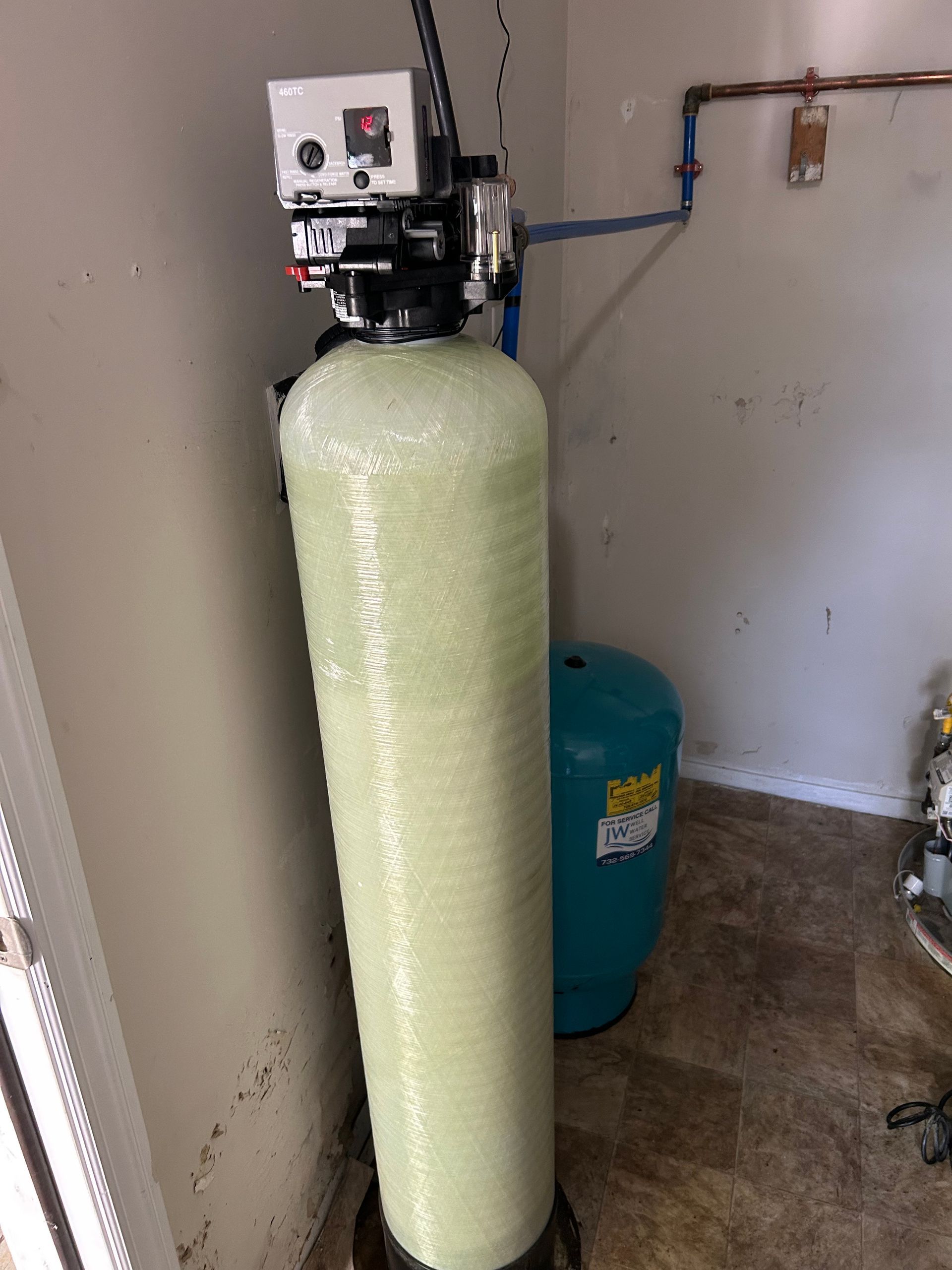 Water filtration system with tall tank and small blue pressure tank in a utility room.