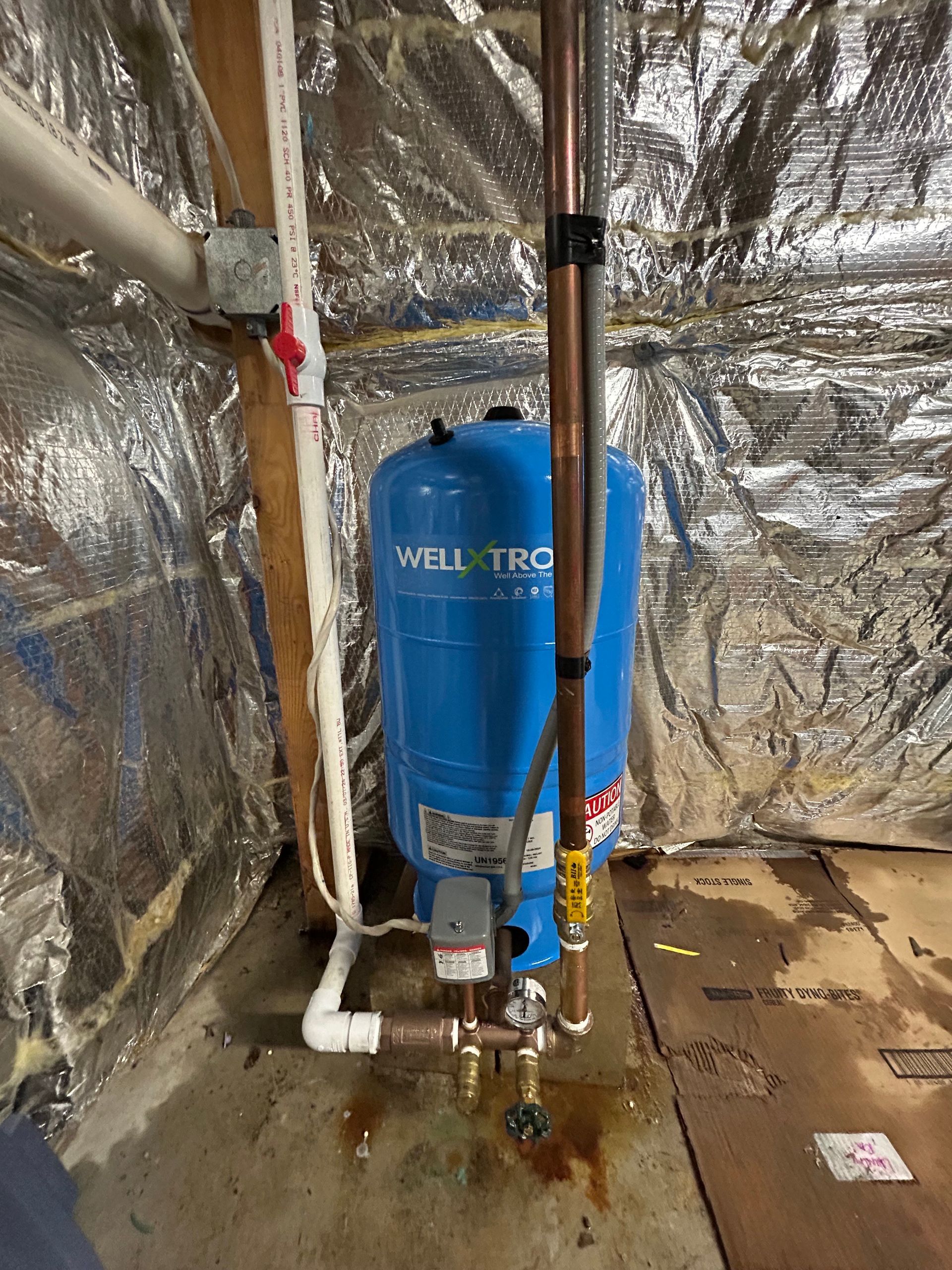 Blue water pressure tank in a utility room with copper pipes and insulation.