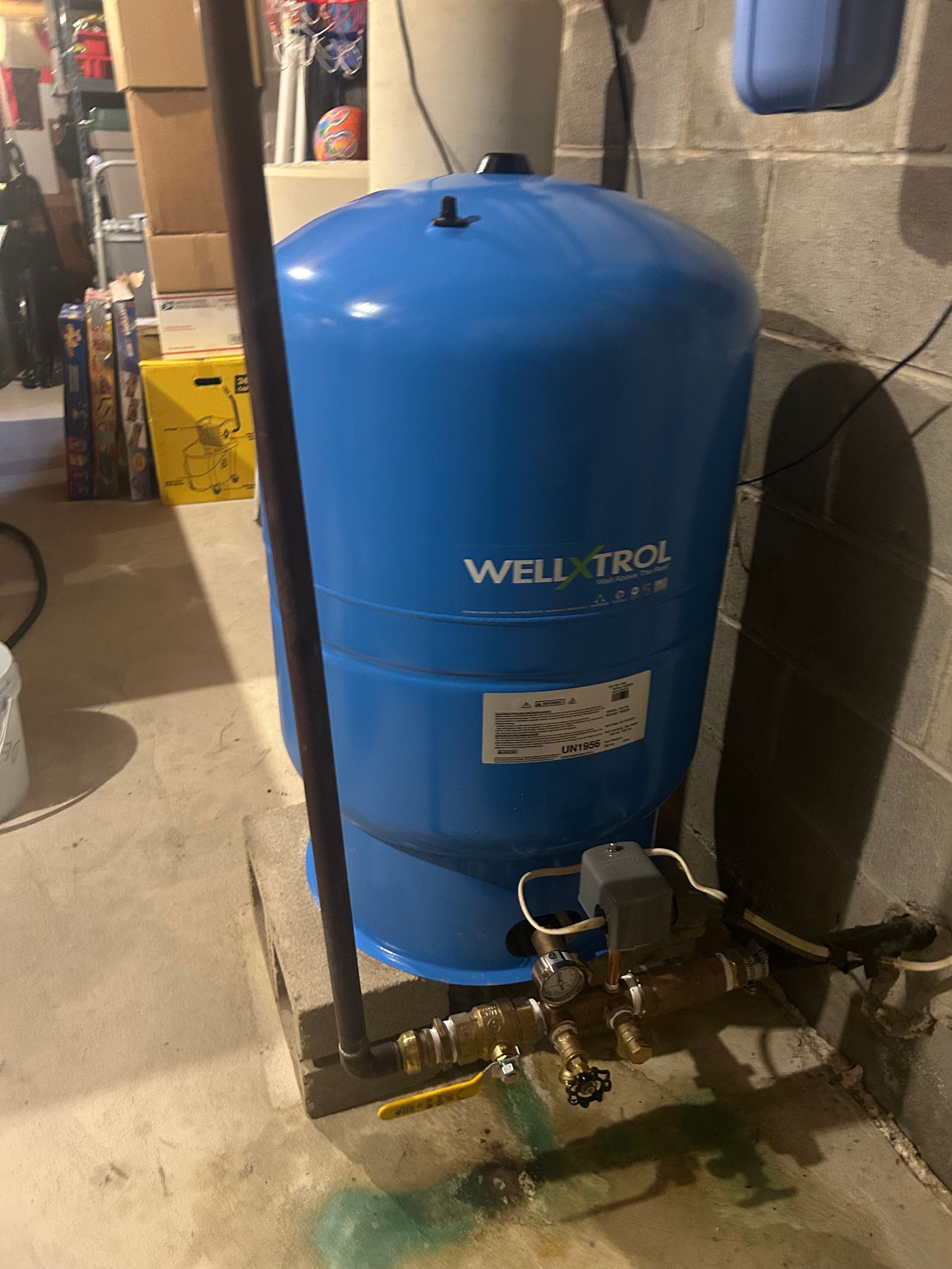 Blue well water tank in a basement setting with pipes and electrical components.