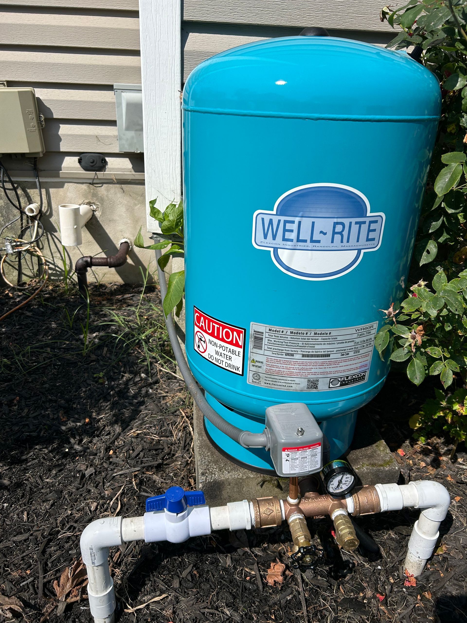 Blue Well-Rite water pressure tank with pipes and gauges outside a building.