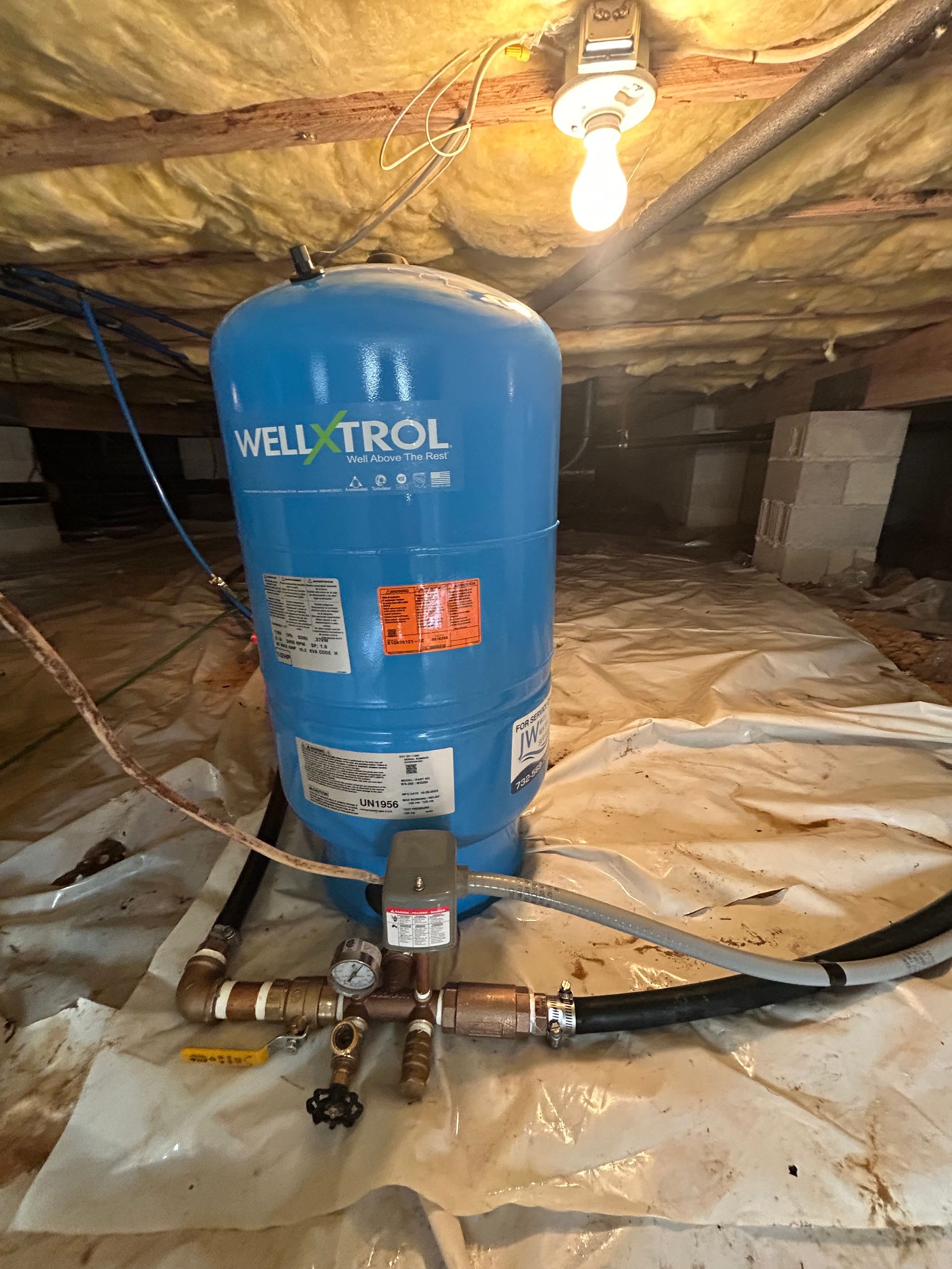 Blue well water tank in a crawlspace with pipes and a lightbulb.