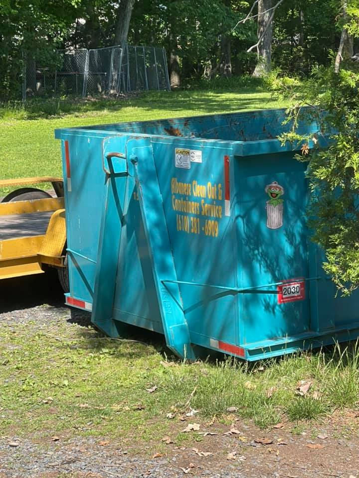 A blue dumpster is parked in the grass next to a yellow trailer.