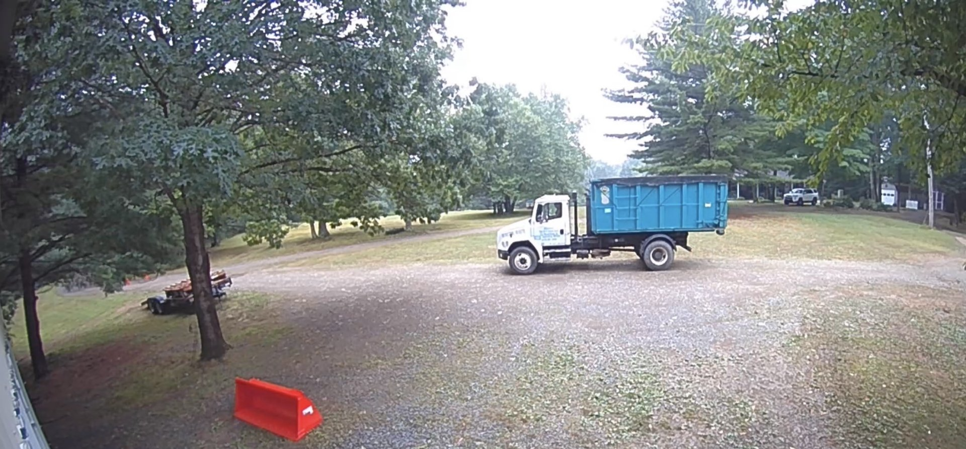 A blue dump truck is parked in a parking lot surrounded by trees.