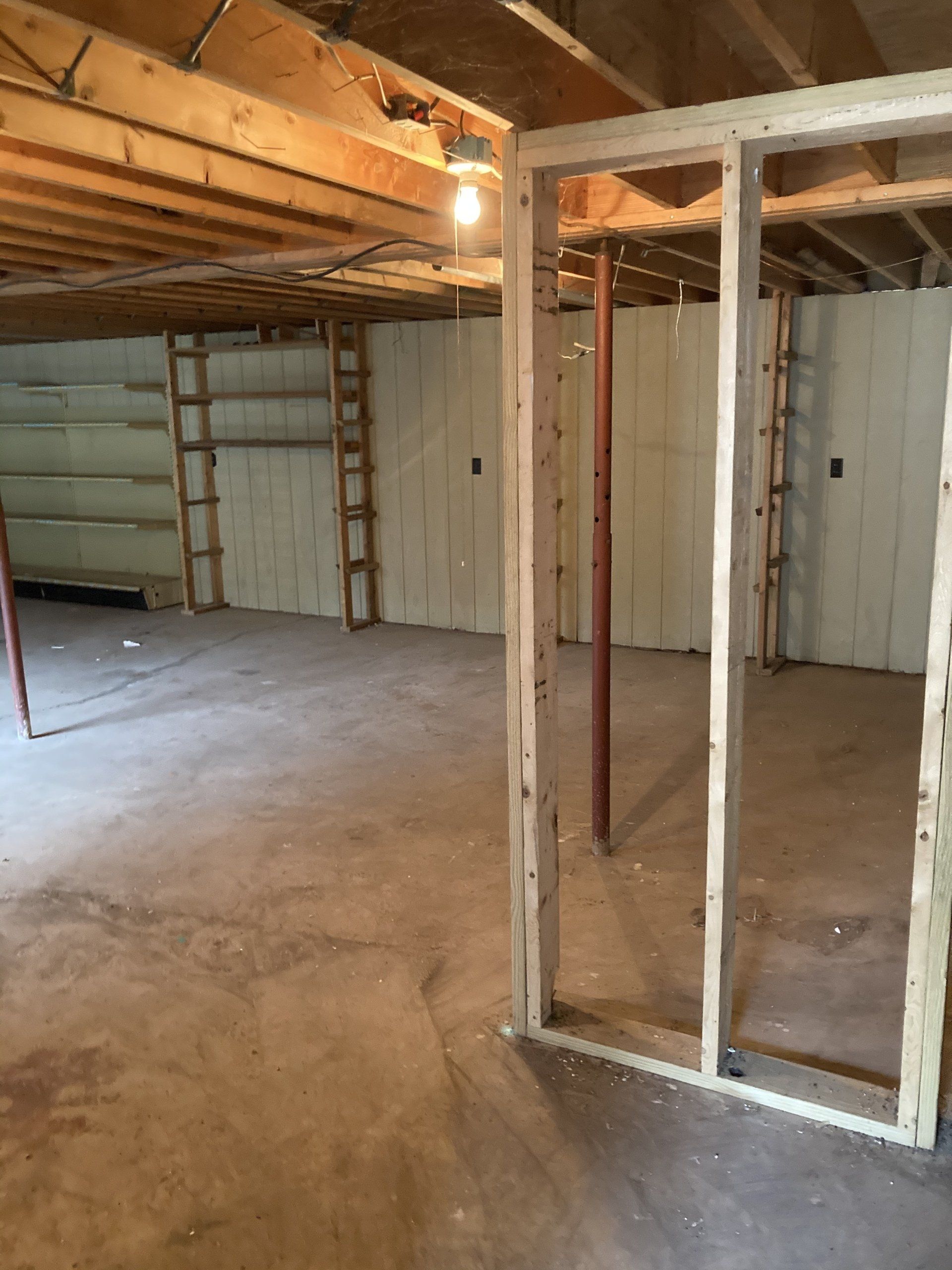 An empty basement with a ladder and a light on the ceiling.