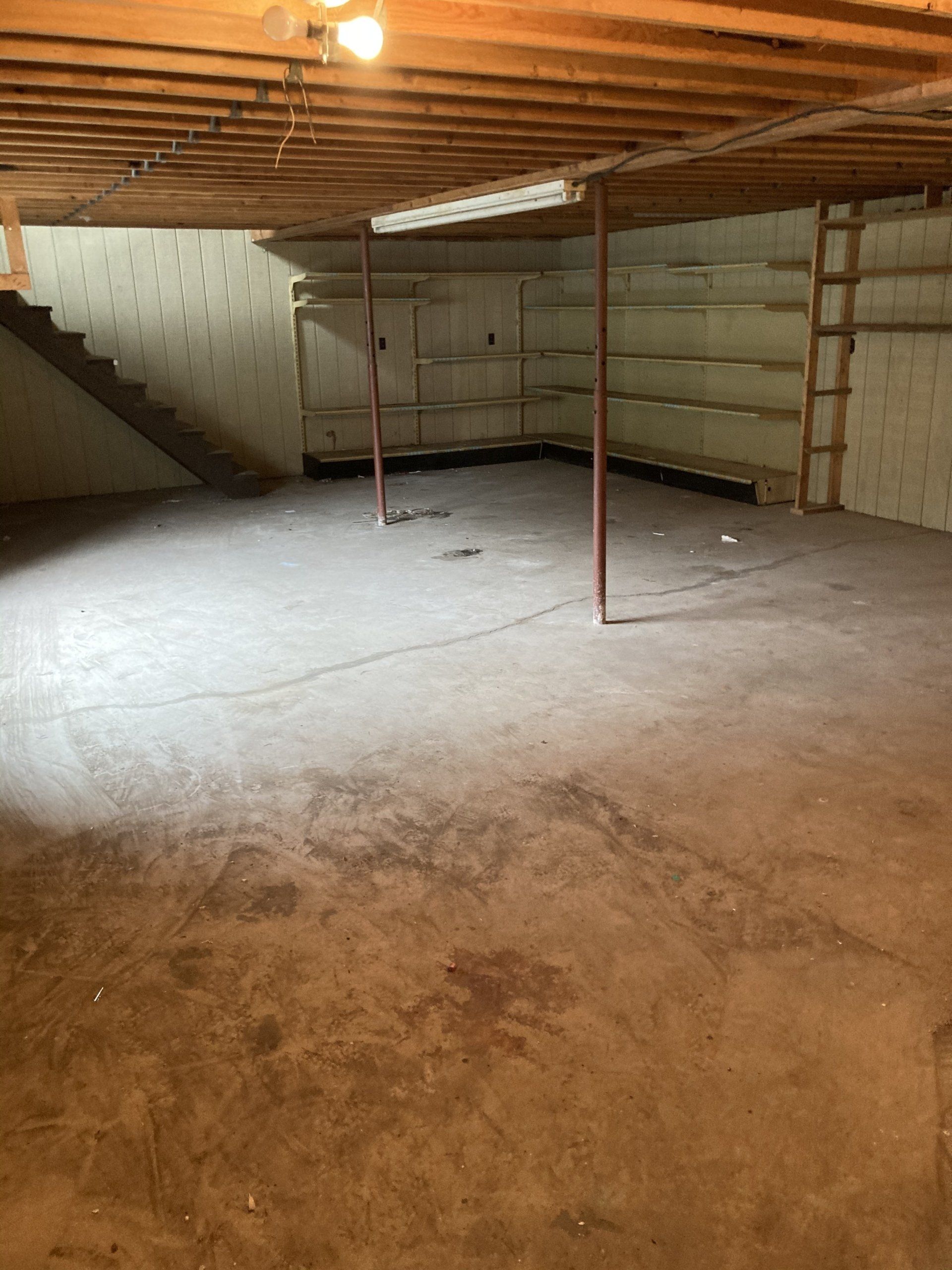 An empty basement with a wooden ceiling and stairs.