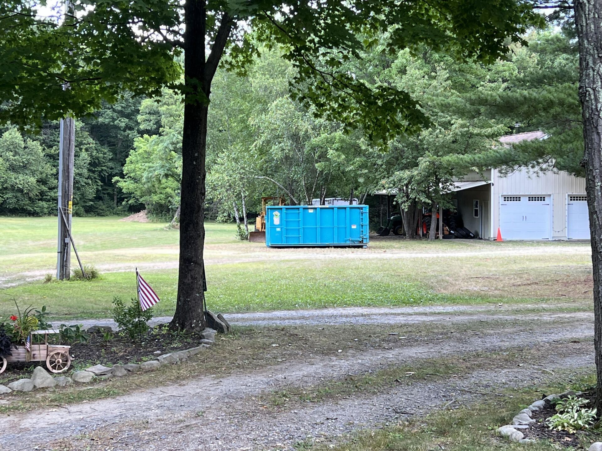 A blue dumpster is sitting in the middle of a grassy field.