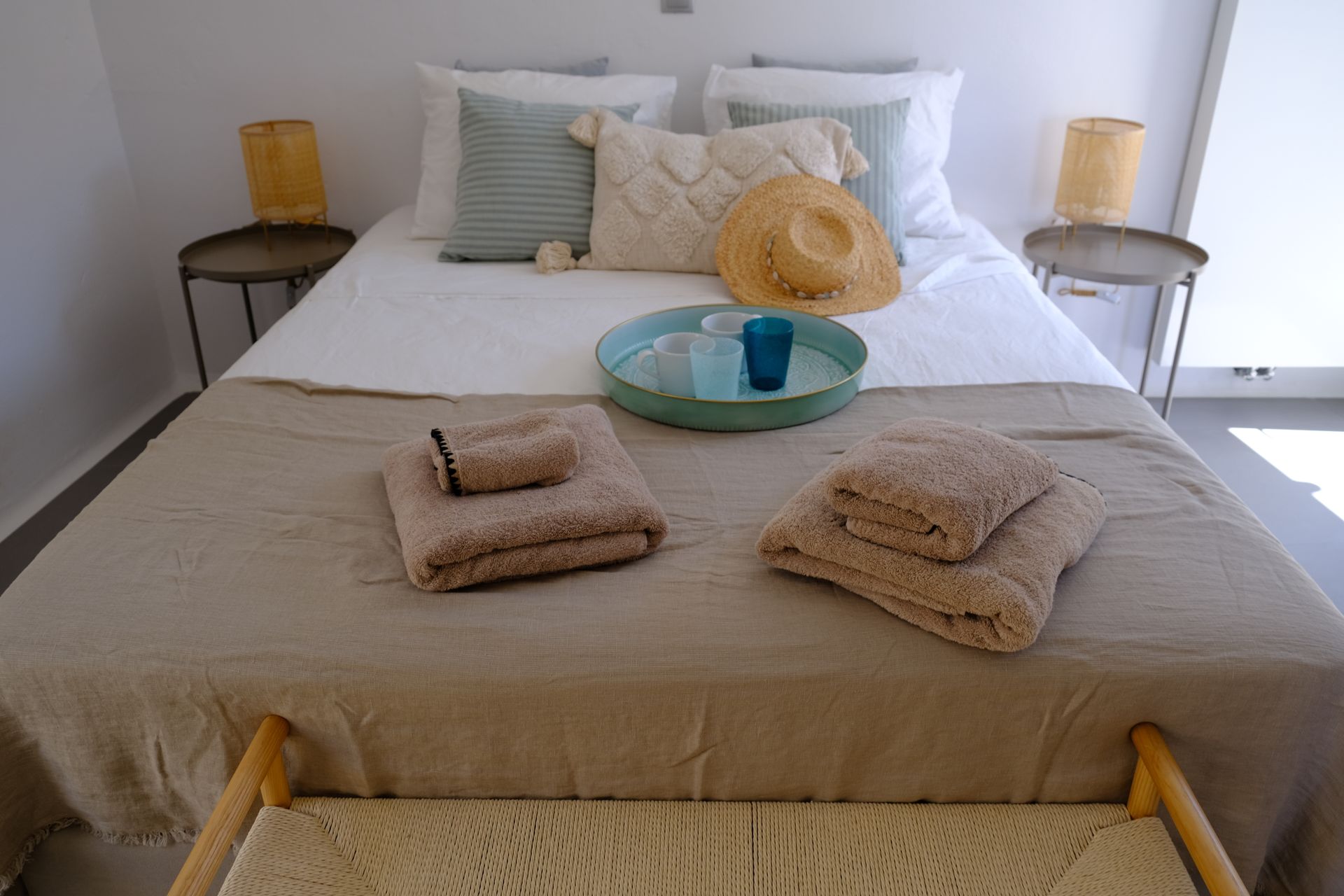 A bed with a tray of towels and a hat on it.