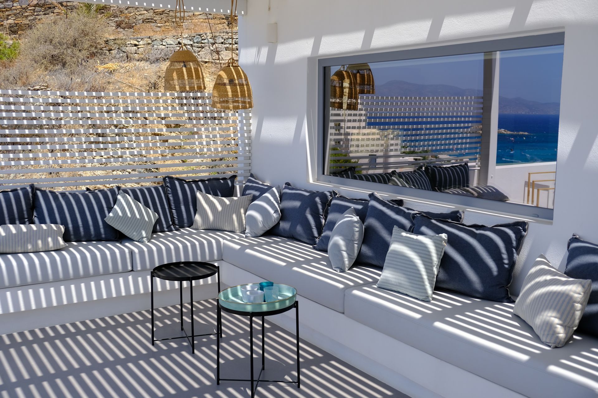 A patio with a couch , two tables and a window overlooking the ocean.