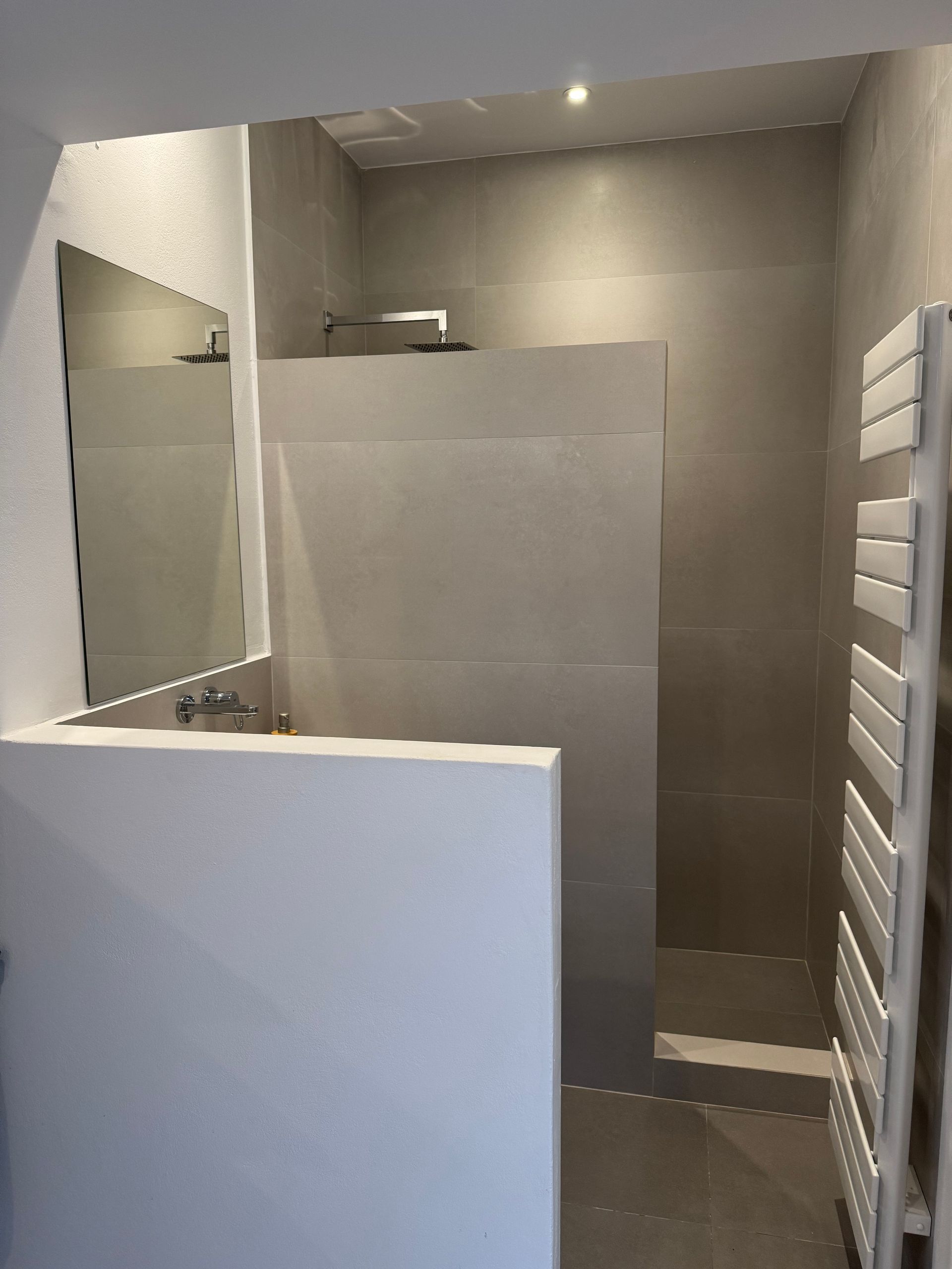 A bathroom with a walk in shower , sink , mirror and towel rack.