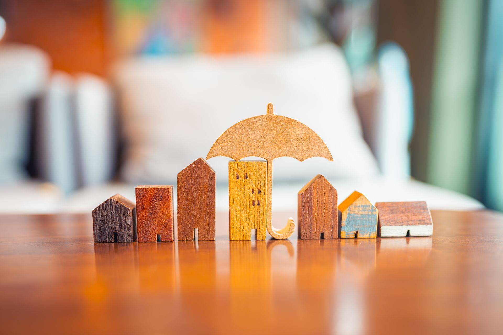 Wooden houses under a wooden umbrella on a reflective wooden surface, symbolizing insurance or protection.