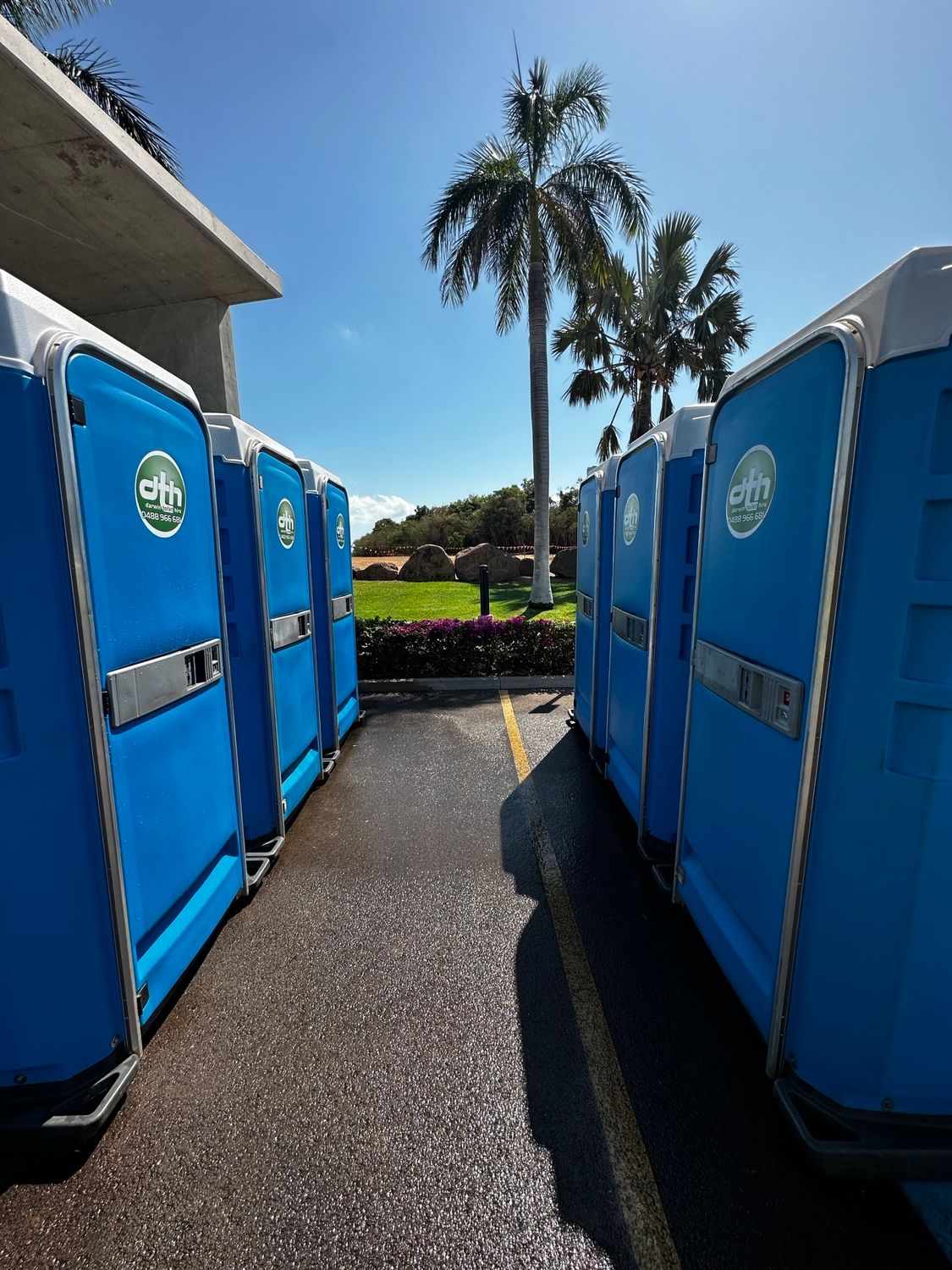 Blue portable toilets lined up on asphalt, palm trees and blue sky in background - Portable toilet hire for hire in Roseberry, NT