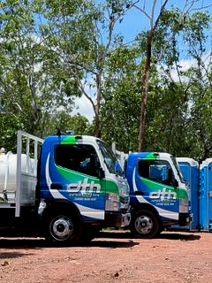 Two blue and white DTH trucks with green accents parked near portable toilets and trees - Portable toilet hire for hire in Roseberry, NT