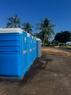 Blue portable toilets lined up outdoors with palm trees and a blue sky in the background - Portable toilet hire for hire in Roseberry, NT