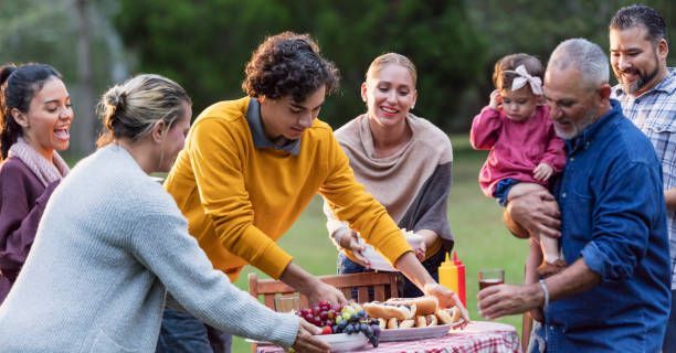 Family gathering around a picnic table outdoors; people are smiling, and serving food.