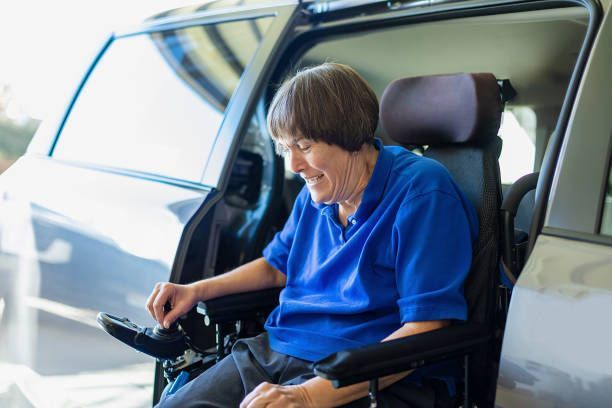 Woman in wheelchair exiting a modified vehicle, wearing blue shirt, smiling.
