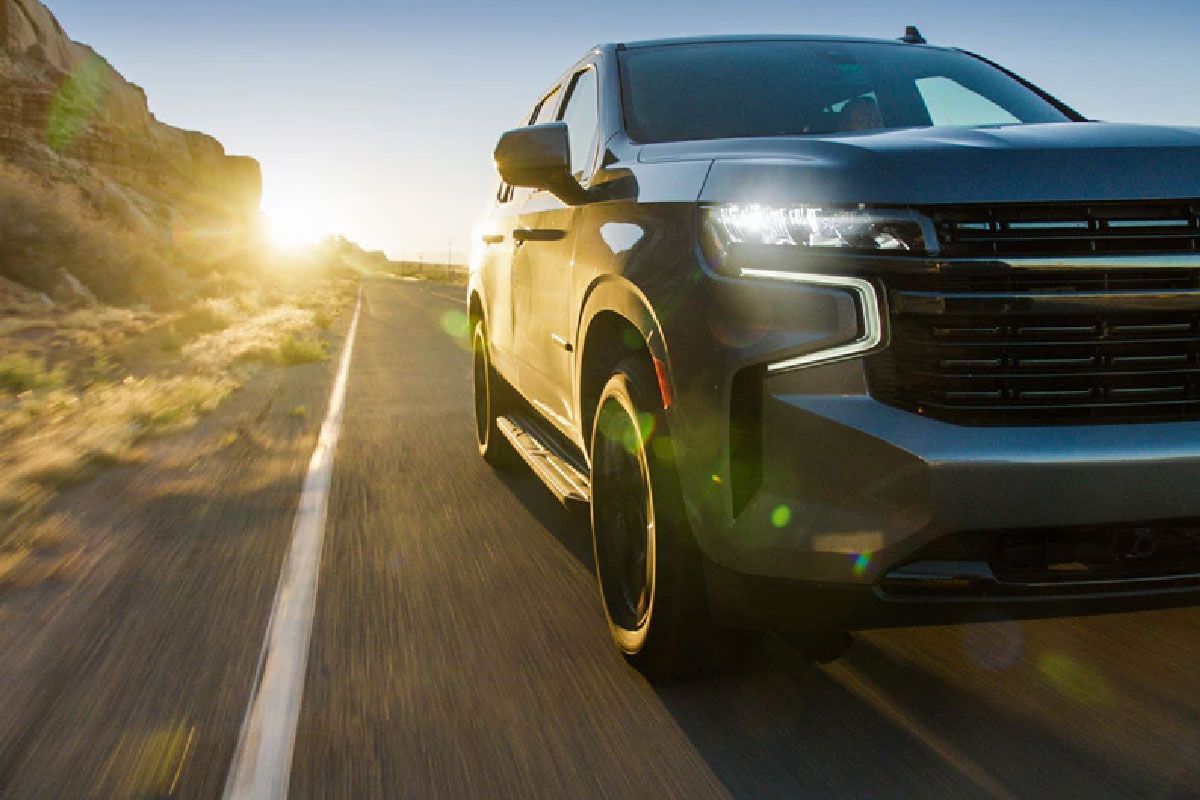 a black suv is driving down a desert road at sunset