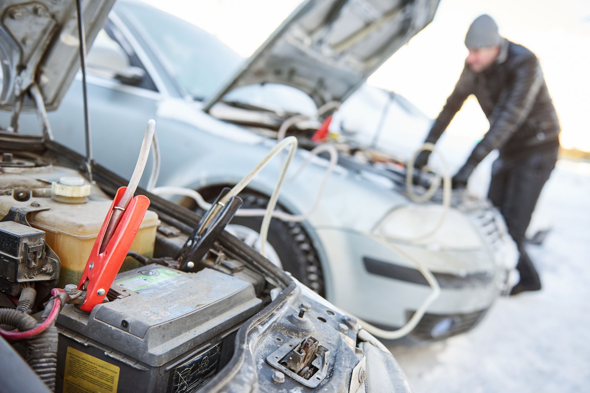 A man is jump starting a car in the snow.