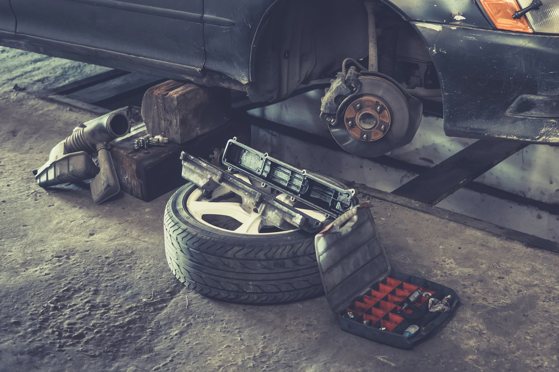 A car is sitting on a lift in a garage with a tire on the ground.