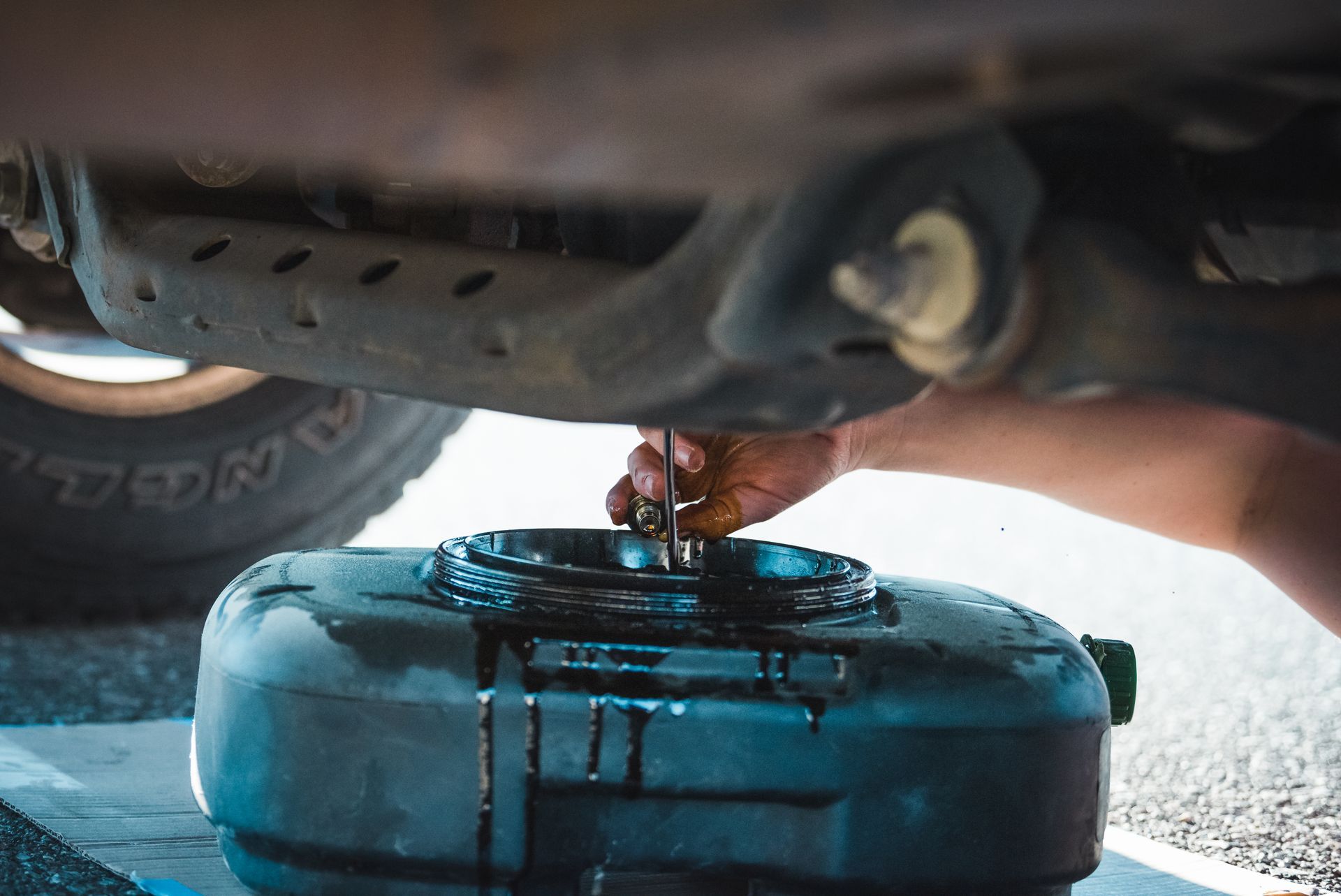 Oil dripping into a blue catch pan under a vehicle during an oil change