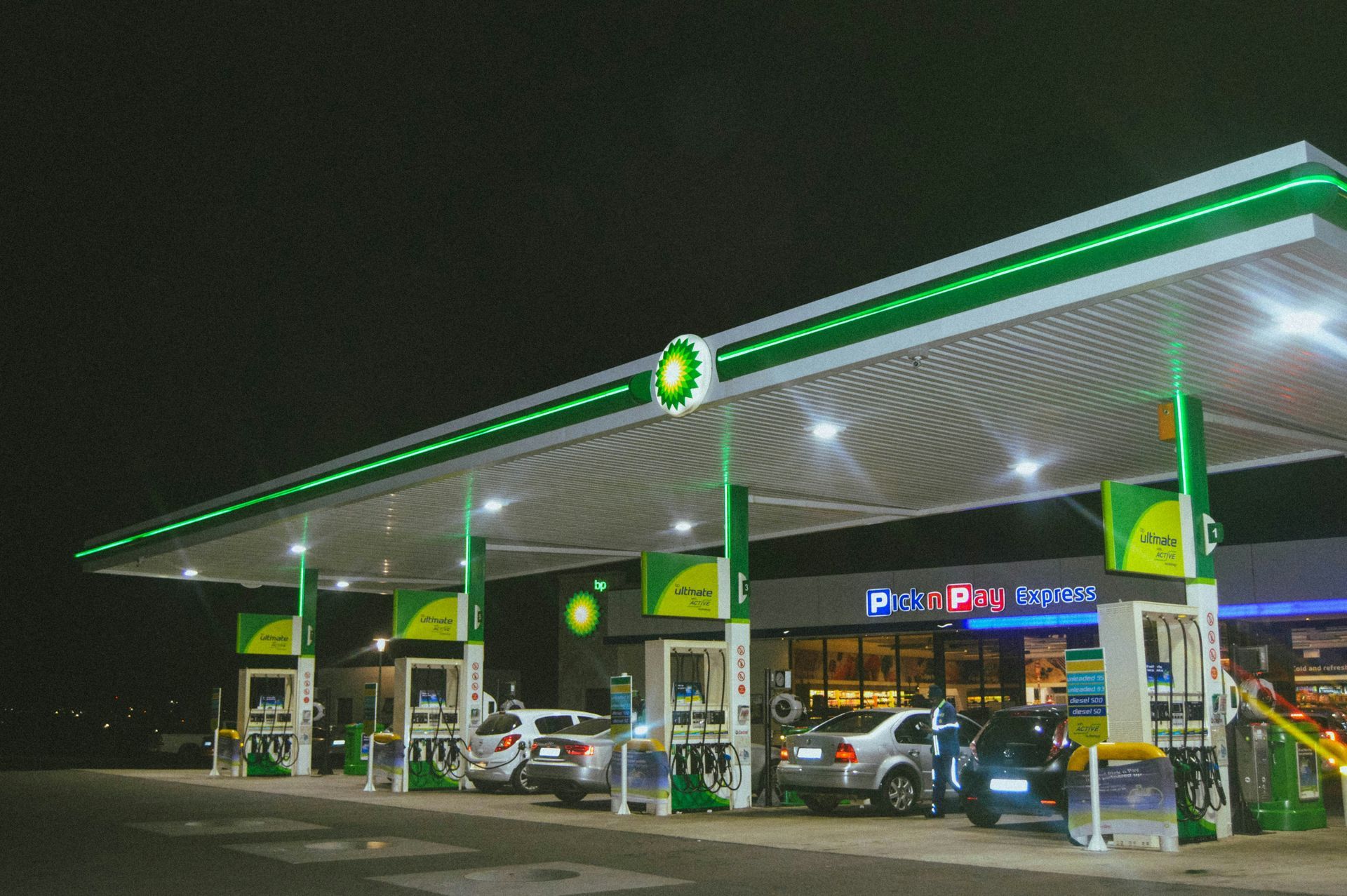 A bp gas station at night with cars parked in front of it.