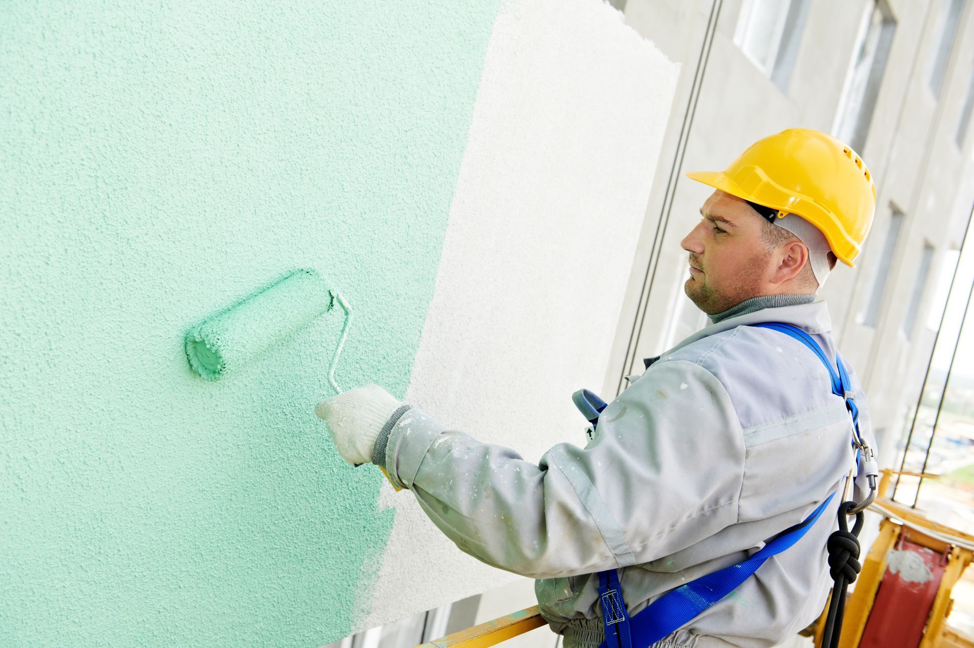 a man wearing a yellow hard hat is painting a wall with a roller
