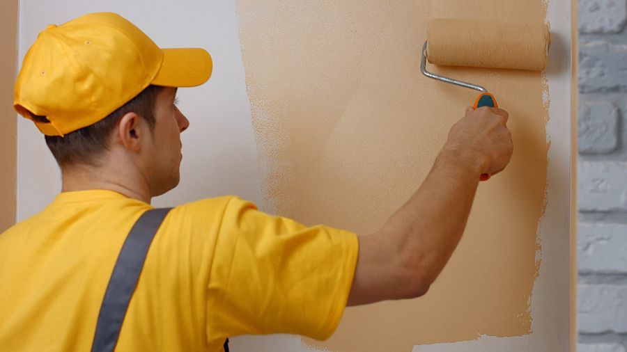 a man in a yellow shirt is painting a wall with a roller