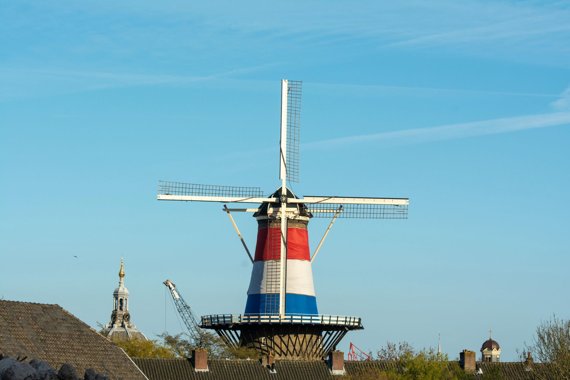 Een Nederlandse windmolen, rood, wit en blauw geschilderd, tegen een blauwe lucht.