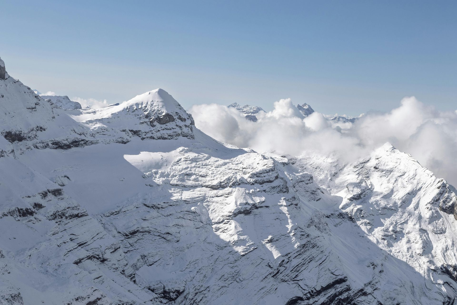 Besneeuwde bergtoppen met hier en daar wolken tegen een helderblauwe hemel.