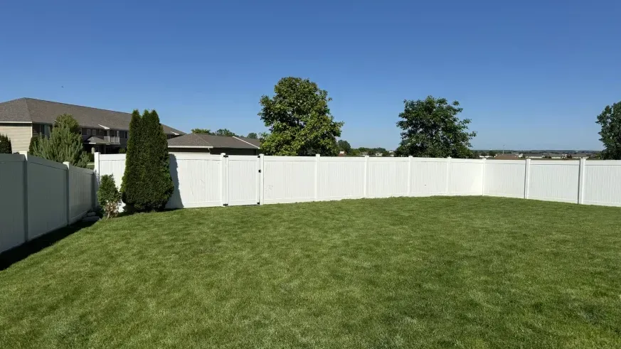 Backyard with green lawn, white fence, and a clear blue sky