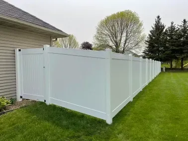 White vinyl privacy fence with gate beside a house on a green lawn