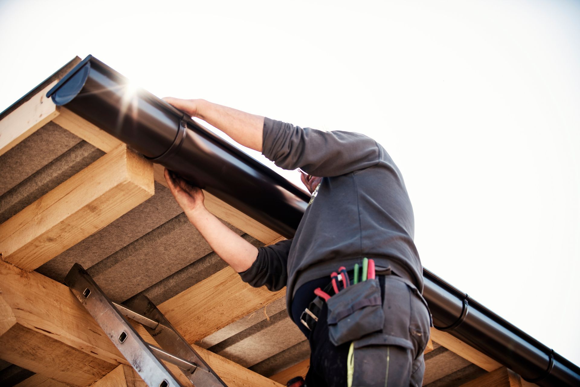 A man is installing a gutter on the roof of a building.