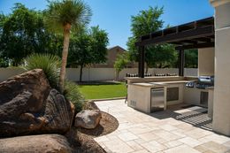 A patio with a grill and a pergola in the backyard