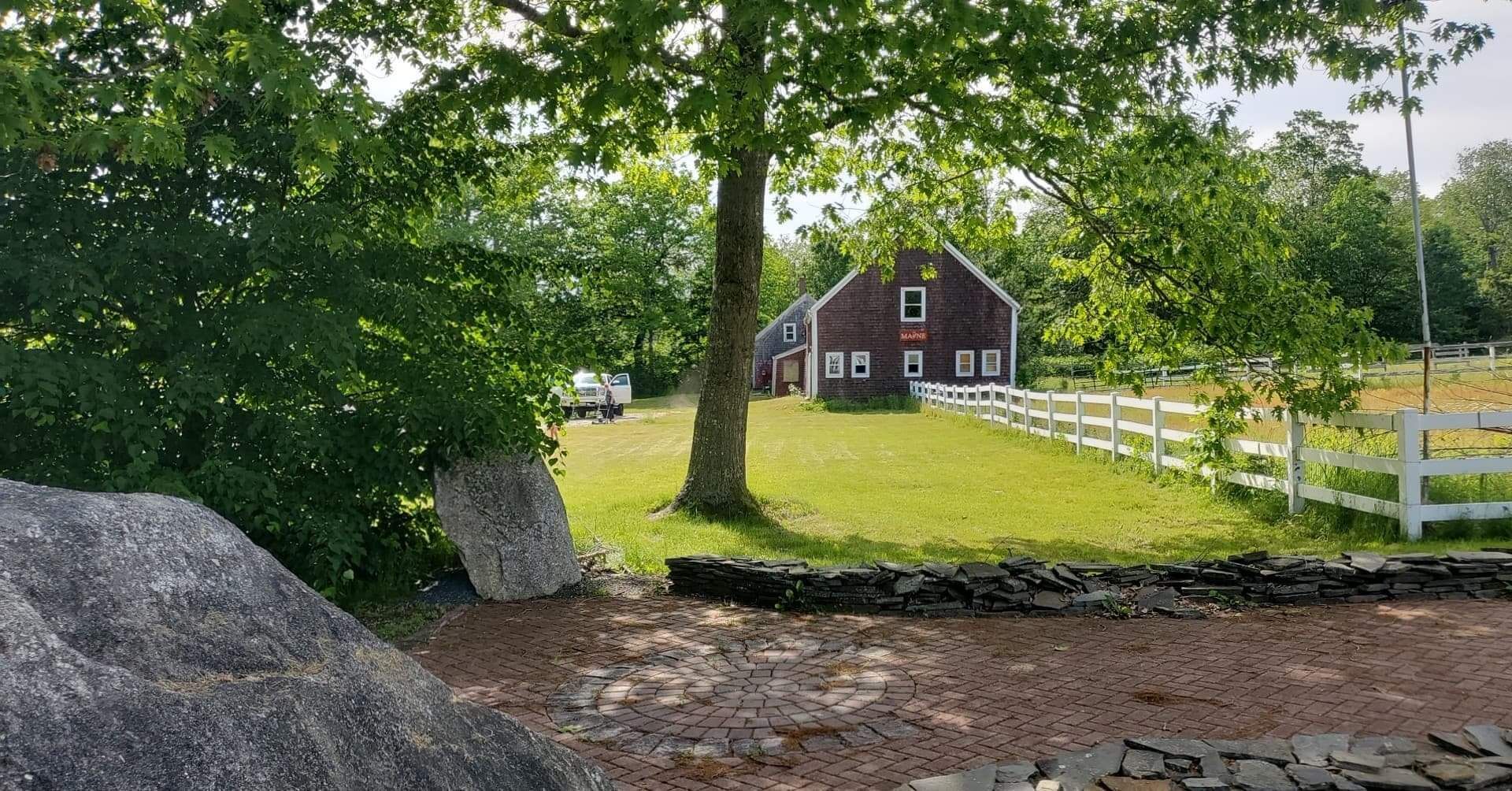 A red barn is surrounded by trees and a white fence.
