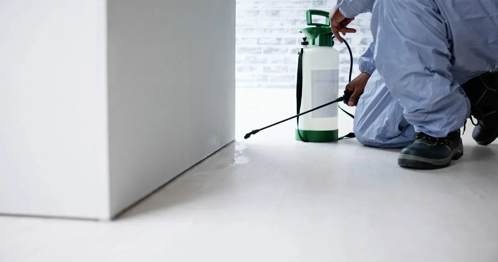 A man is kneeling down on the floor spraying a bottle of chemicals.