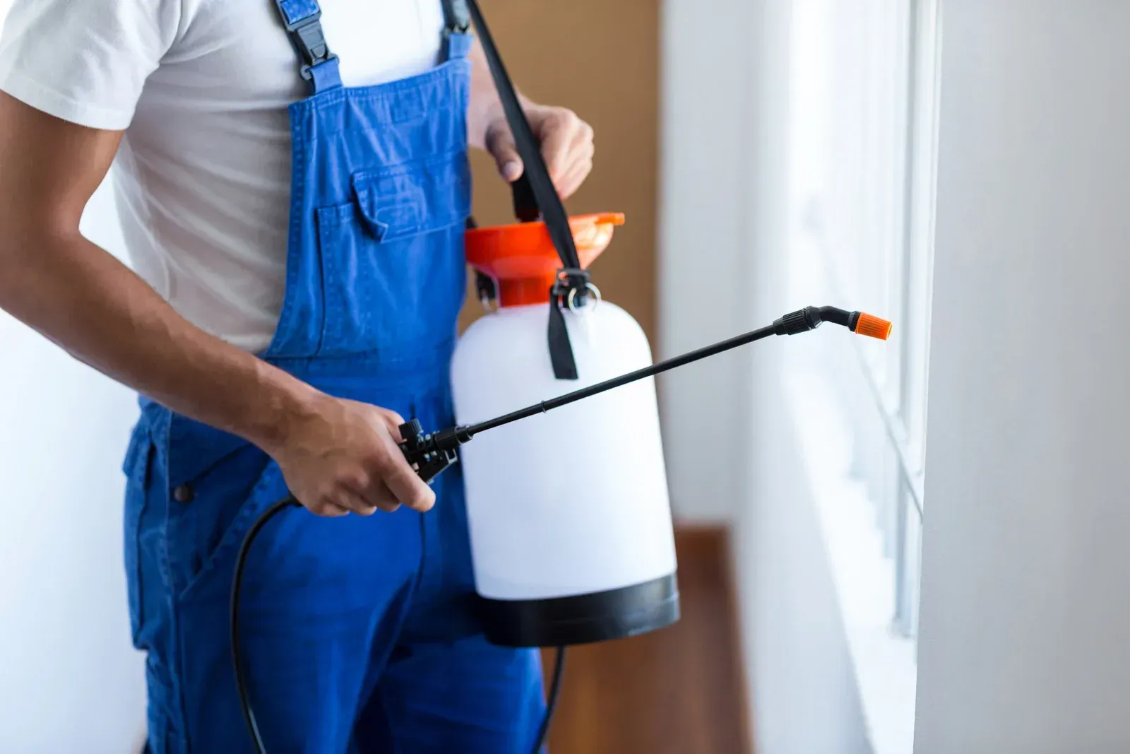 A man in blue overalls is spraying a room with a spray bottle.