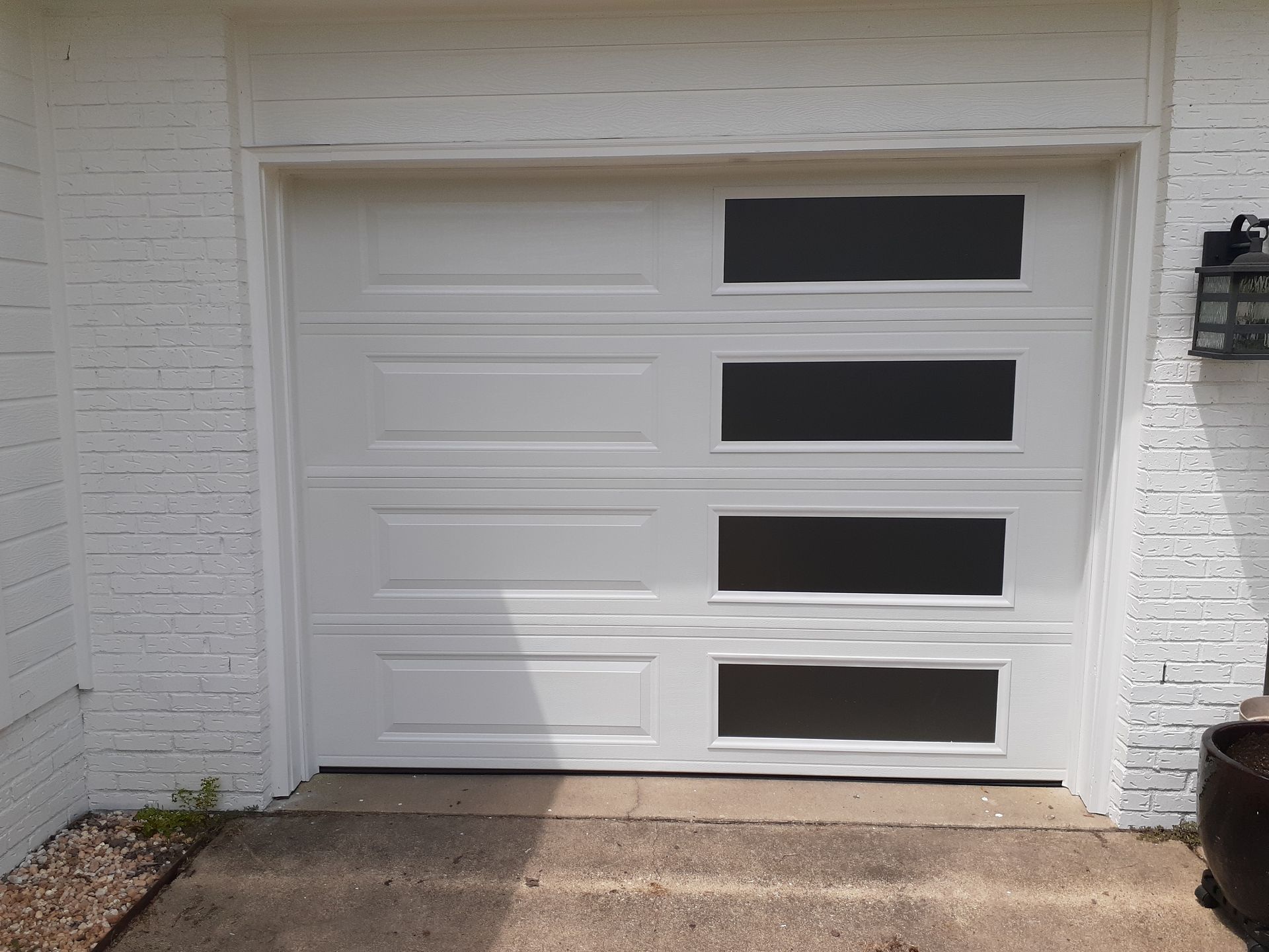 a white garage door with black windows on a white brick wall .