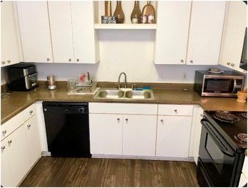 A kitchen with white cabinets , a black dishwasher , a microwave , and a sink.