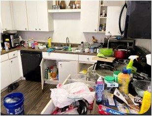 A kitchen with a lot of cleaning supplies and a bucket on the counter.