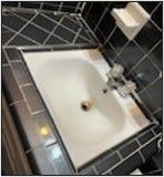 A bathroom sink with black tiles and a drain.